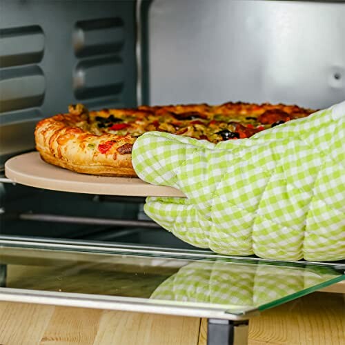 Pizza being placed in oven with green checkered oven mitt.
