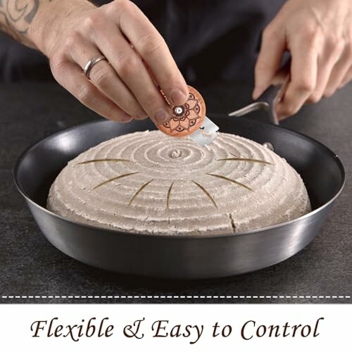 Person scoring bread dough with a tool in a pan. 