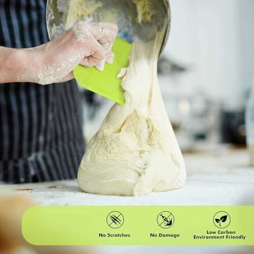 Person using a green scraper to knead dough on a floured surface.